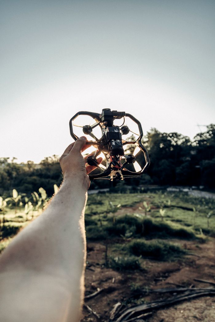 A close-up of a person holding a drone, with a rural landscape backdrop, capturing the sunrise.